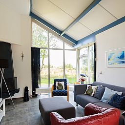 Ruime woonkamer in Duinvilla 6, een bungalow in Hollum, Ameland, met grote ramen en uitzicht op de natuurlijke omgeving van de Waddeneilanden.