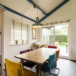 Gezellige eetkamer in Duinvilla 6, een bungalow in Hollum op Ameland, met een rustgevend uitzicht op de tuin en kleurrijke stoelen rondom de tafel.