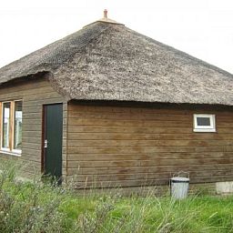 Buitenzijde van houten vakantiehuis De Vijfhoek in Nes, Ameland met rieten dak.