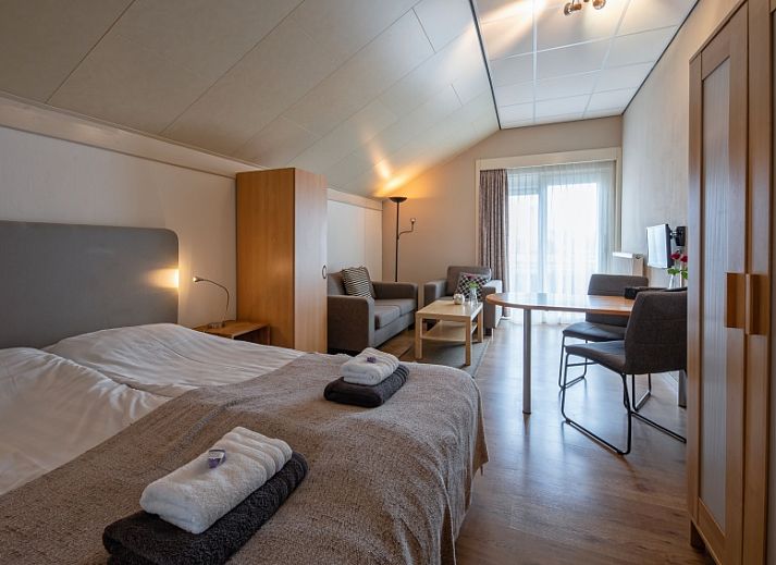 Geraeumiges Schlafzimmer im Ferienhaus Typ 1 - 2100 in De Cocksdorp, Texel, mit bequemem Bett und Sitzecke.