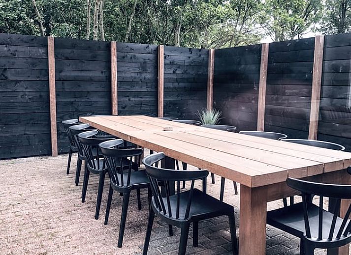 Hinterer Garten und Terrasse des Ferienhauses in De Cocksdorp, Texel, mit grossen Rasenflaechen.