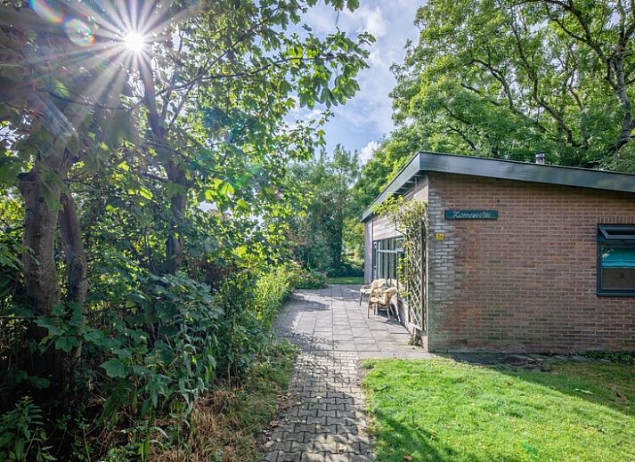 Ferienhaus De Zonneweelde in De Koog, Texel, umgeben von ueppiger Natur und Sonnenlicht auf der Terrasse.