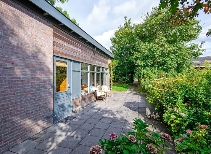 Ferienhaus De Zonneweelde in De Koog, Texel, umgeben von ueppiger Natur und Sonnenlicht auf der Terrasse.