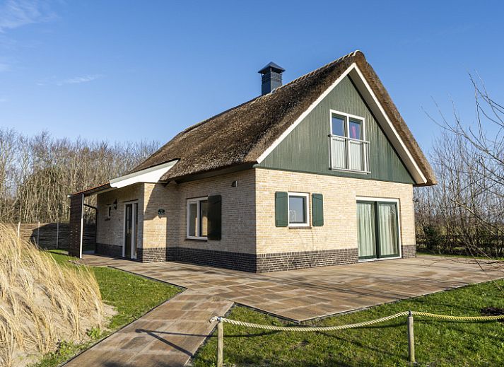 De Abeel vacation home with thatched roof in De Koog, Texel, surrounded by red flowers and dunes.