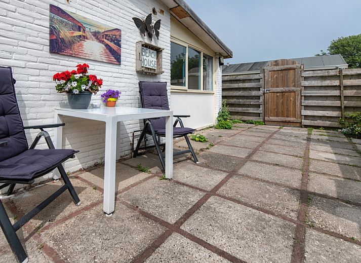 Sonnige Terrasse des Ferienhauses 2490 in De Koog, Texel, mit bequemen Stuehlen und dekorativen Blumenkuebeln.