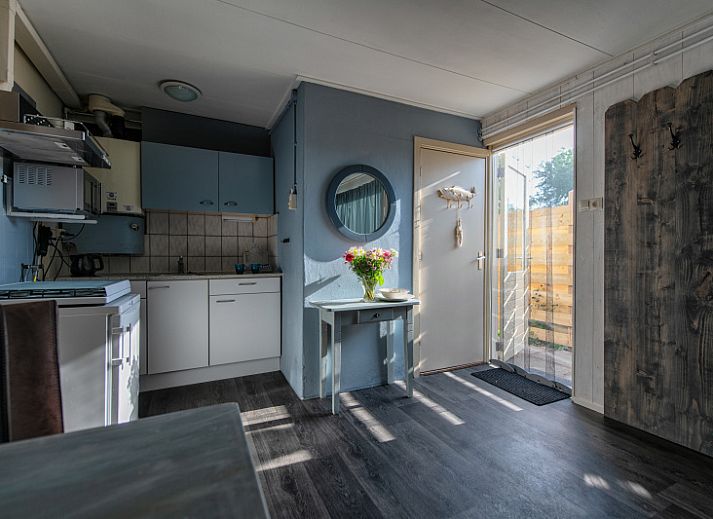 Sonnige Terrasse des Ferienhauses 2490 in De Koog, Texel, mit bequemen Stuehlen und dekorativen Blumenkuebeln.