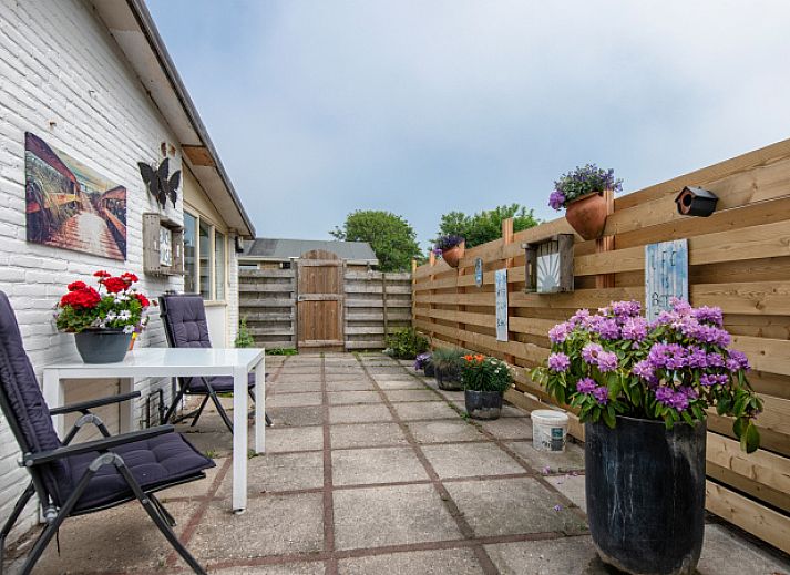 Sonnige Terrasse des Ferienhauses 2490 in De Koog, Texel, mit bequemen Stuehlen und dekorativen Blumenkuebeln.
