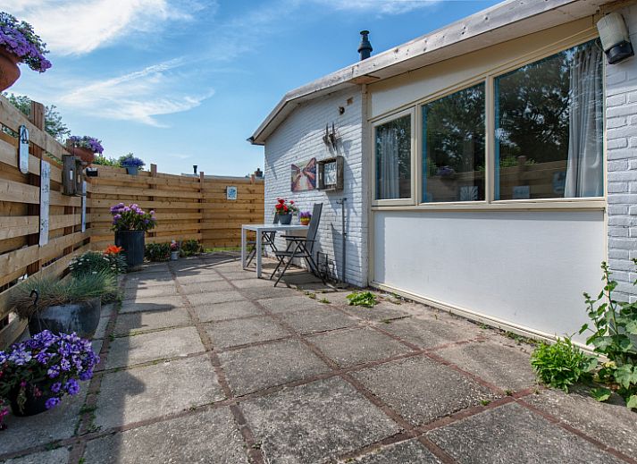 Sonnige Terrasse des Ferienhauses 2490 in De Koog, Texel, mit bequemen Stuehlen und dekorativen Blumenkuebeln.