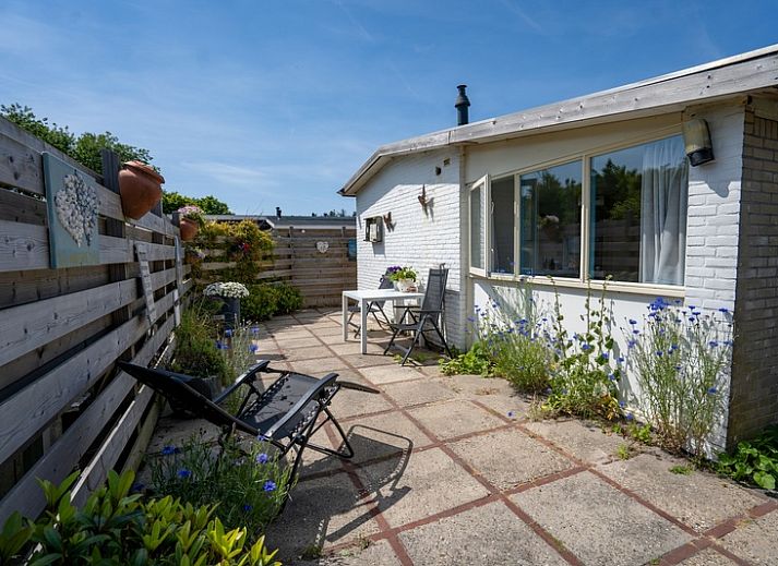 Geraeumige Terrasse am Ferienhaus 2490 in De Koog, Texel, umgeben von einem Holzzaun und bunten Blumen.