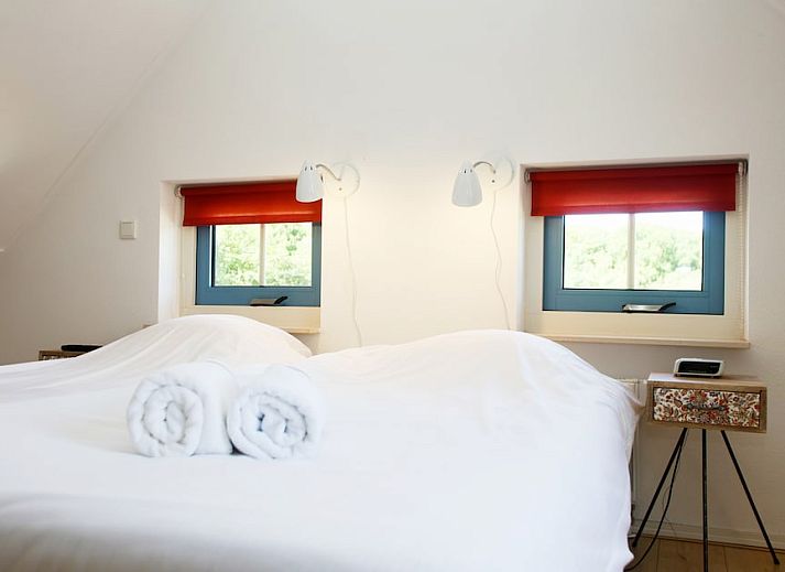 Gezellige woonkamer in bungalow T8A, De Koog, Texel met comfortabele rode bank en houtkachel, ideaal voor ontspanning op de Waddeneilanden.