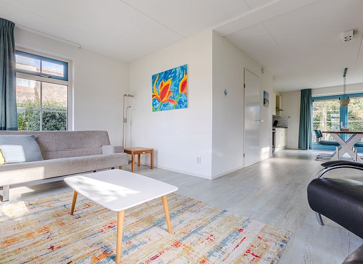 Charmante bungalow T6AB in De Koog, Texel, met rieten dak en blauwe deur, omgeven door natuurlijke tuin en rustieke houten omheining.