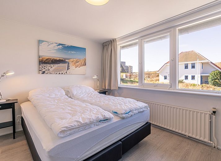 Gemuetliches Wohnzimmer in De Zandduyn, De Koog, Texel, mit rotem Sofa und grossen Fenstern fuer natuerliches Licht.