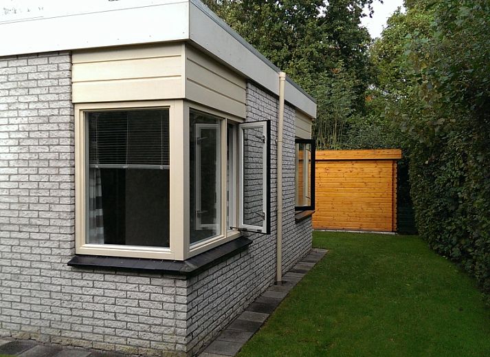 Side view of Bungalowpark De Noordel - De Polderdijkjes in Oosterend, Texel. Vacation home with green hedges and access path.