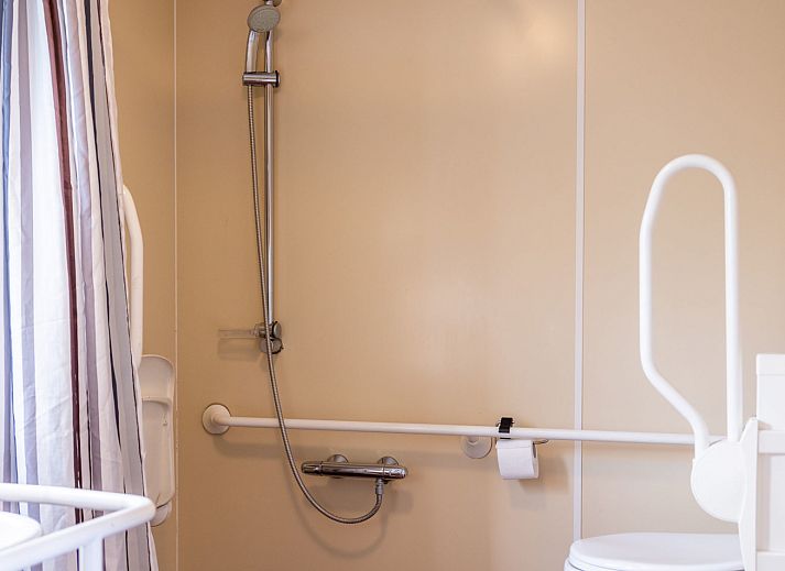 Veranda des Duinbungalows Mindervalide in Oosterend, Terschelling, mit bequemen Stuehlen und Sonnenschirm.