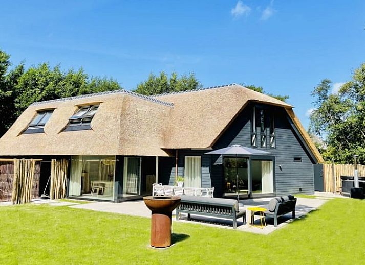 Charmant vakantiehuisje in Ballum met rieten dak, Ameland, omgeven door groen.