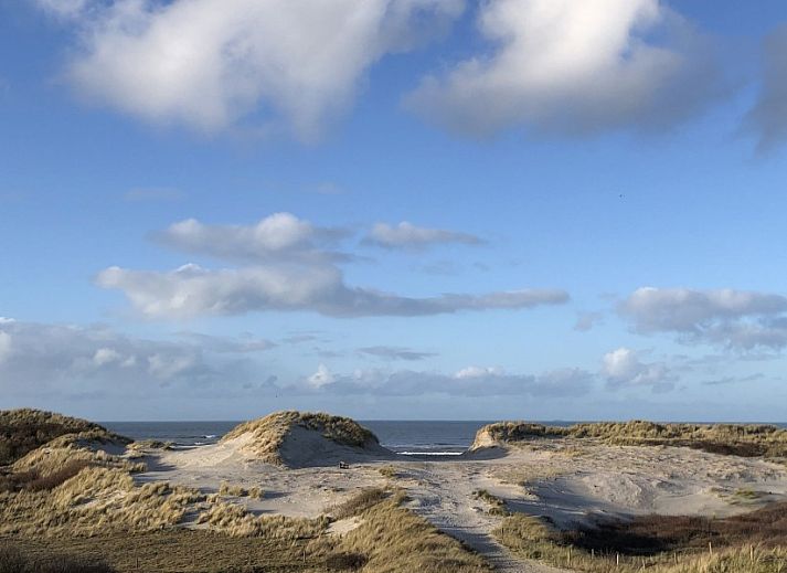 Dining area in vacation home Naar Zee, Buren, Ameland with wooden table and colorful chairs.