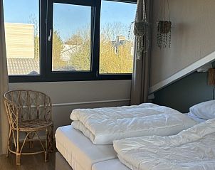 Lichte slaapkamer in Vakantiehuis aan de golfbaan, De Cocksdorp Texel, Waddeneilanden, met raam en houten stoel.