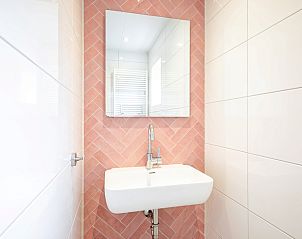 Waschbecken mit Spiegel im Ferienhaus Slufterduin 134, De Cocksdorp Texel mit rosa gefliester Wand.