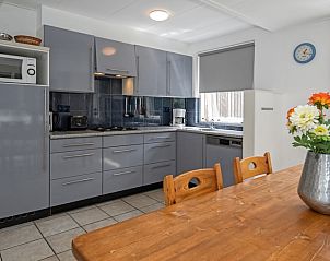 Kche und Essbereich des Ferienhauses Slufterduin 098, Texel, mit Blumen auf dem Tisch und Zugang zur Terrasse.