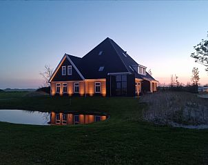 Illuminated vacation home Eierland in De Cocksdorp, Texel, with reflection in the pond during dusk.