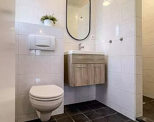 Moderne badkamer in Huisje in De Cocksdorp, Texel, met strakke witte tegels en houten wastafelmeubel.