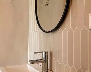 Moderne wastafel in Huisje in De Cocksdorp, Texel, met stijlvolle tegelwand en ronde spiegel.