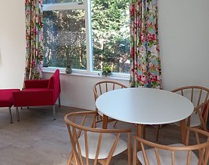 Dining area in Huisje Quirijn, De Koog Texel with round table and wooden chairs surrounded by colorful curtains.