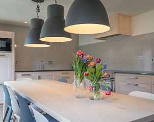 Cozy dining area in vacation home Orchismient 24, De Koog, Texel, with flowers on the table and hanging lamps.