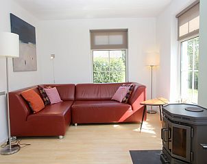 Gezellige woonkamer in bungalow T8A, De Koog, Texel met comfortabele rode bank en houtkachel, ideaal voor ontspanning op de Waddeneilanden.