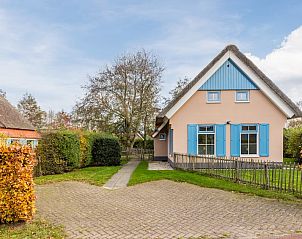 Charmante bungalow T6AB in De Koog, Texel, met rieten dak en blauwe deur, omgeven door natuurlijke tuin en rustieke houten omheining.