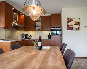 Dining area and kitchen of Villa 304 in De Koog, Texel with stylish wooden table for cozy meals.