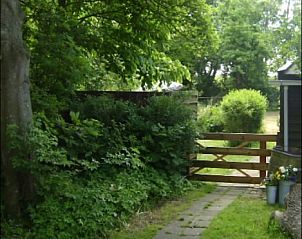 Rustieke tuinpad met houten poort bij De Fazant, vakantiehuis in Oosterend, Texel, omgeven door weelderige natuur.