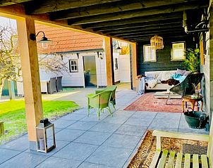 Gemtliche Veranda im Ferienhaus in Oosterend, Texel, mit bequemen Sitzgelegenheiten und Blick auf den Garten.