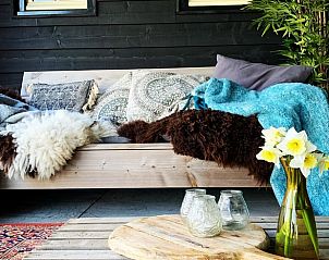 Stilvolle Sitzecke auf der Veranda des Ferienhauses in Oosterend, Texel, mit weichen Decken und Kissen.