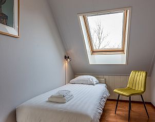 Knusse eenpersoons slaapkamer in Daalder vakantiehuis, Oosterend, Texel, met dakraam en comfortabele stoel.