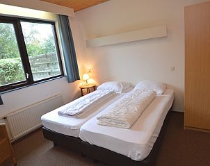 Slaapkamer in vakantiehuis Narcis, De Dennen, Texel met comfortabele bedden en tuinzicht.