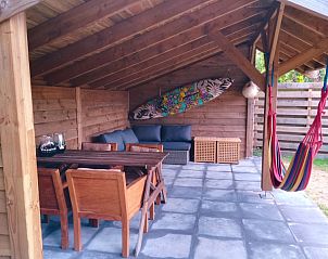 Overdekt terras bij Vakantiepark De Koorn-aar - Chalet 102 type C, De Dennen, Texel, met houten meubilair en hangmat.