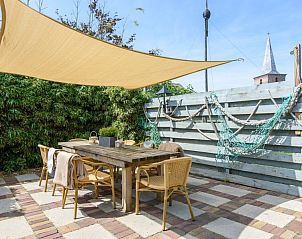 Zonnig terras van De Sjouw, Hoorn, Terschelling, met schaduwdoek en houten eettafel.