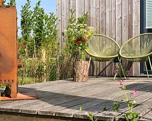 Veranda van Buitenhuis chalet in Midsland Noord, Terschelling, met moderne stoelen en bloemen.