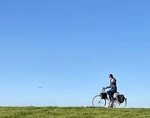 Fietser op dijk nabij Esti bungalow, Ballum, Ameland met blauwe lucht.