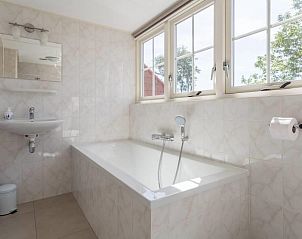 Luxe badkamer in Weigelia vakantiehuis, Ballum, Ameland met ligbad en grote ramen met uitzicht op de natuur.