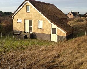 Zijaanzicht van In Het Dal vakantiehuis in Buren, Ameland, met rieten dak en natuurlijke omgeving.