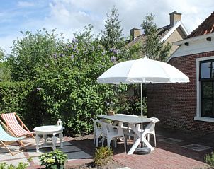 Zonnig terras van Opa's huis, vakantieaccommodatie Schiermonnikoog, met tuinmeubilair en parasol.