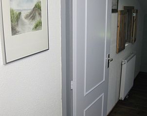 Gang in vakantiehuis Adje op Schiermonnikoog met kunst aan de muur en houten vloer.