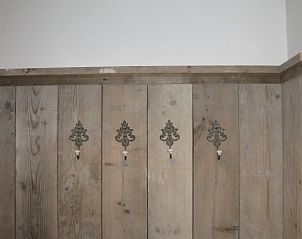 Rustieke kapstok in vakantiehuis Adje op Schiermonnikoog met houten afwerking en decoratieve haken.